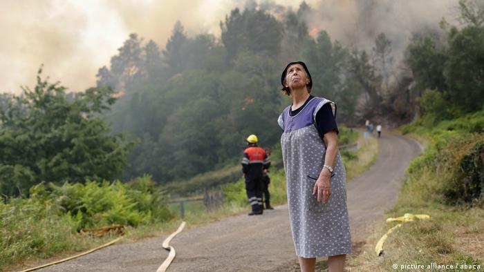 A resident of Samos, near Lugo, looks to the sky with fire smoke behind her