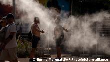 Two men cool themselves with water from a public sprinkler on a hot and sunny day in Barcelona, Spain, Saturday, July 16, 2022. Many European countries are facing exceptional heat this month also attributed to climate change. (AP Photo/Emilio Morenatti)