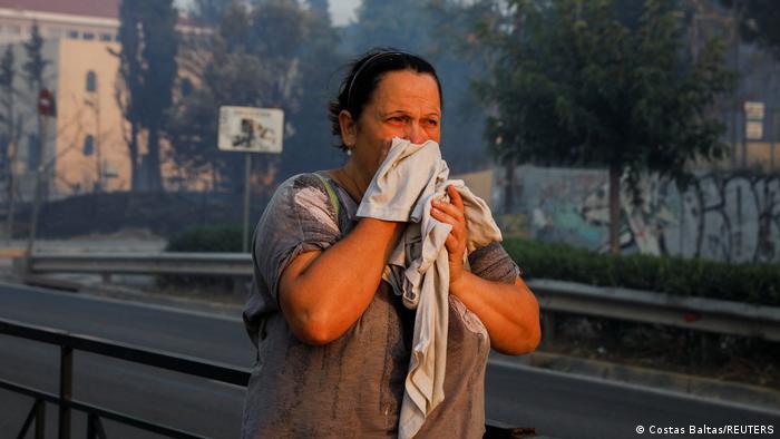 A woman covers her face as a wildfire burns in Pallini, near Athens, Greece 