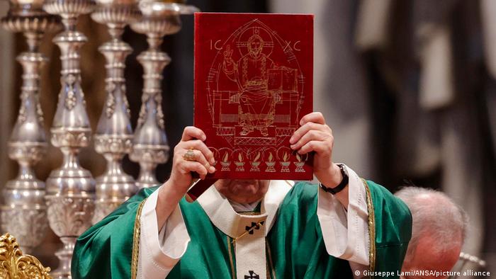 Pope Francis, dressed in green vestments, holds up a red and gold-bound Bible with an embossed image of Christ Pantocrator on its cover