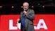 Lula fala ao microfone em frente a painel vermelho com seu nome Lula fala ao microfone em frente a painel vermelho com seu nome