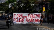 Residents walk holding a banner with a message that reads in Portuguese: Out from the favela killer police, after a police operation that resulted in multiple deaths, in the Complexo do Alemao favela in Rio de Janeiro, Brazil, Thursday, July 21, 2022. Police said in a statement it was targeting a criminal group in Rio largest complex of favelas, or low-income communities, that stole vehicles, cargo and banks, as well as invaded nearby neighborhoods. (AP Photo/Silvia Izquierdo)