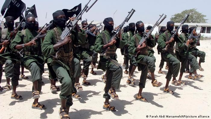 Al-Shabab fighters raise right leg and hold up guns during military exercize