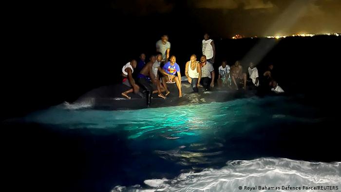 Survivors of a migrant boat that capsized perch on the overturned vessel off the coast of New Providence island.