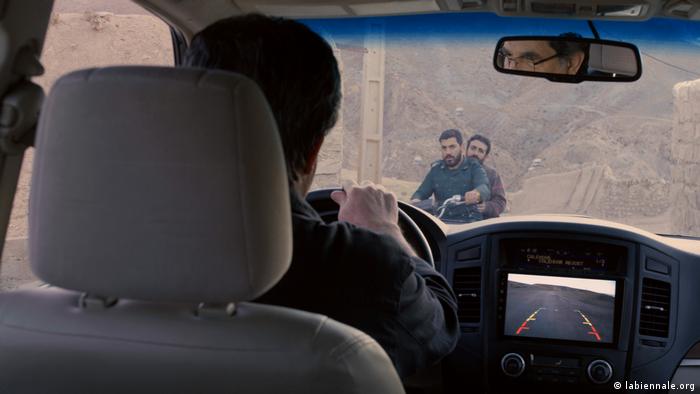 Filmstill von Khers Nist: Ein Autofahrer schaut durch die Windschutzscheibe auf zwei auf einem Motoroller sitzenden Personen