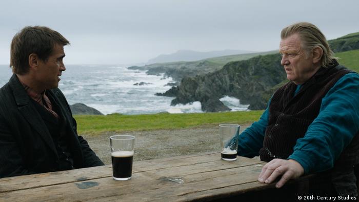 Colin Farrell und Brendan Gleeson sitzen in eine Filmszene an einem Tisch und trinken Bier