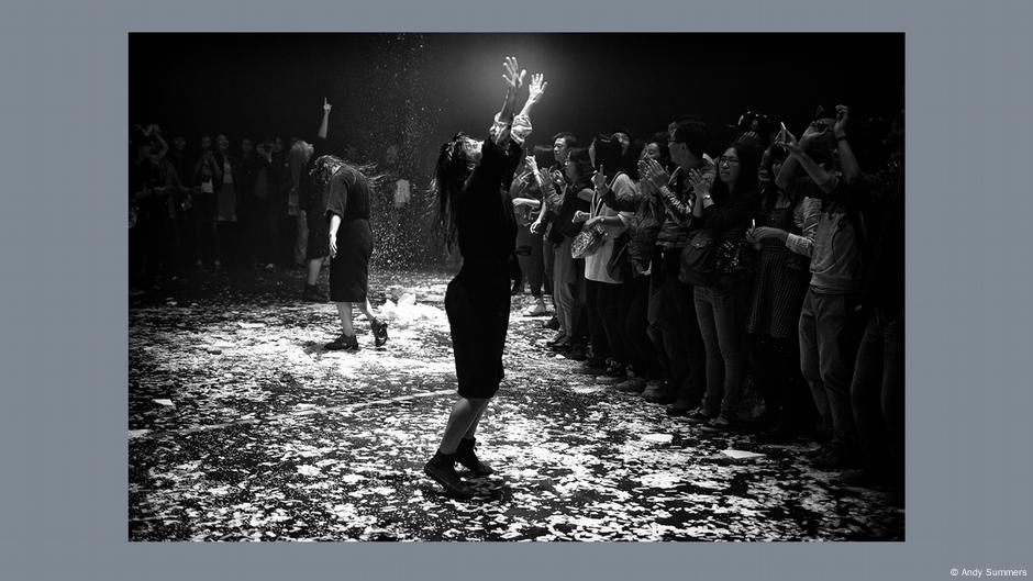 Andy Summers A Certain Strangeness in Wetzlar, a crowd of people, one woman stands apart, hands high in the air 