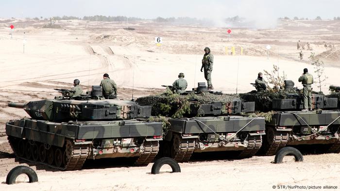 Nato-Übung in Polen. Drei Leopard-Panzer der polnischen Armee stehen bei einer Übung nebeneinander und sind von hinten zu sehen. Auf den Panzern stehen Soldaten