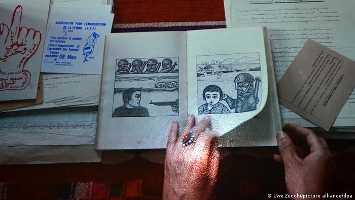 Eine Hand blättert in einer Broschüre, in der Bleistift-Zeichnungen zu sehen sind. Sie zeigen israelische Soldaten, einer greift ein Kind am Ohr. 