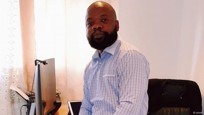 David Ndikumana with a thick beard and blue shirt sitting next to his desk and computer