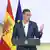 Spanish Prime Minister Pedro Sanchez speaks at a podium without a tie