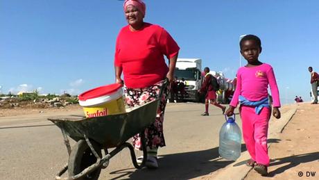 A woman and a girl carry water from delivery truck in Gqeberha, South Africa