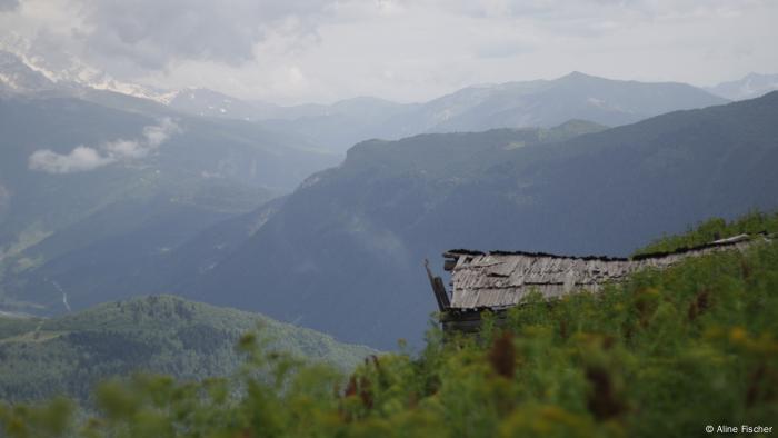 A derelict hut is visible in the foreground, with tall mountains rising in the back.