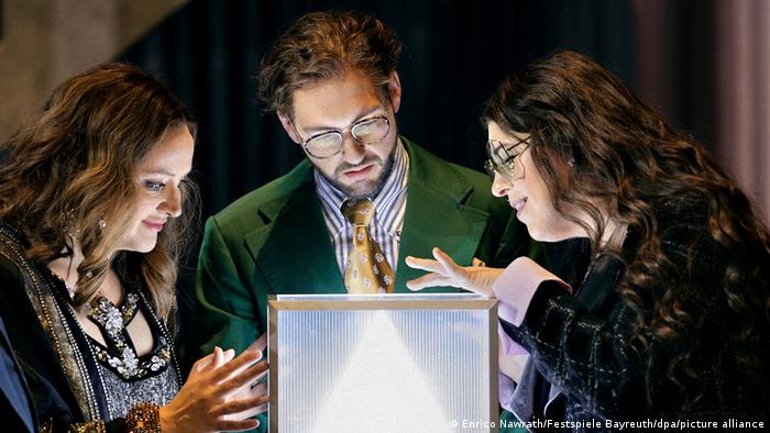 Three people look at a model of a glowing pyramid.