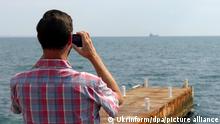 Мужчина фотографирует сухогруз Razoni с украинским зерном, покидающий порт Одессы