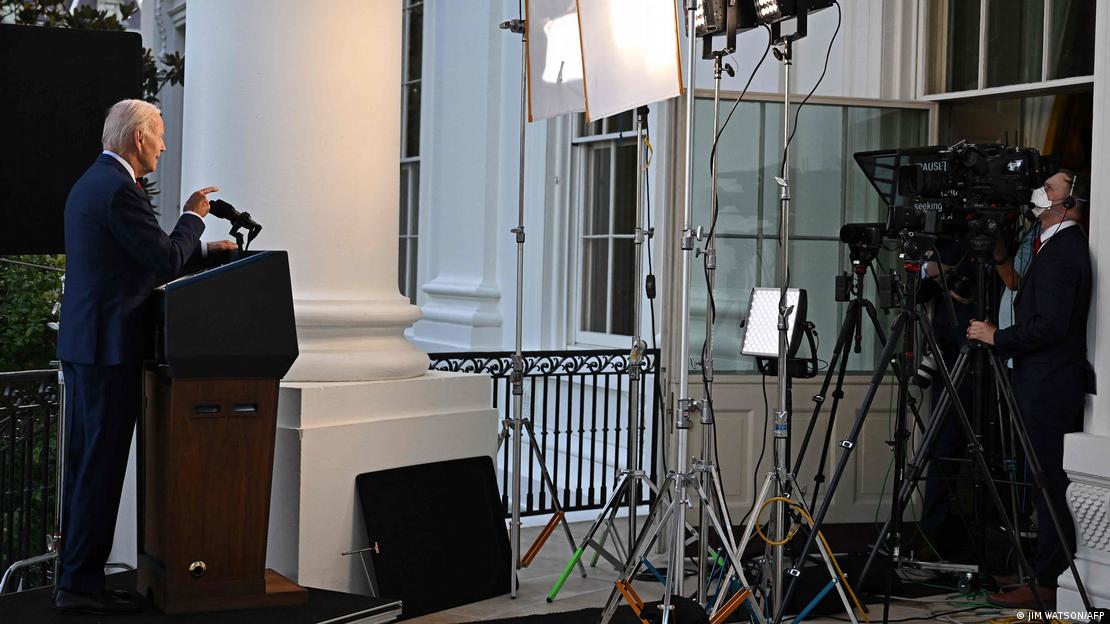 O presidente americano Joe Biden fala durante uma gravação para anunciar que o líder da Al Qaeda foi morto em operação dos EUA. Ele está à esquerda na foto, de lado, apontando para a câmera. A foto mostra uma sala com câmeras e luzes onde Biden grava a mensagem.