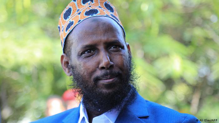 Muktar Robow Abu-Mansur wears hat and blue sports coat and appears to smile slightly