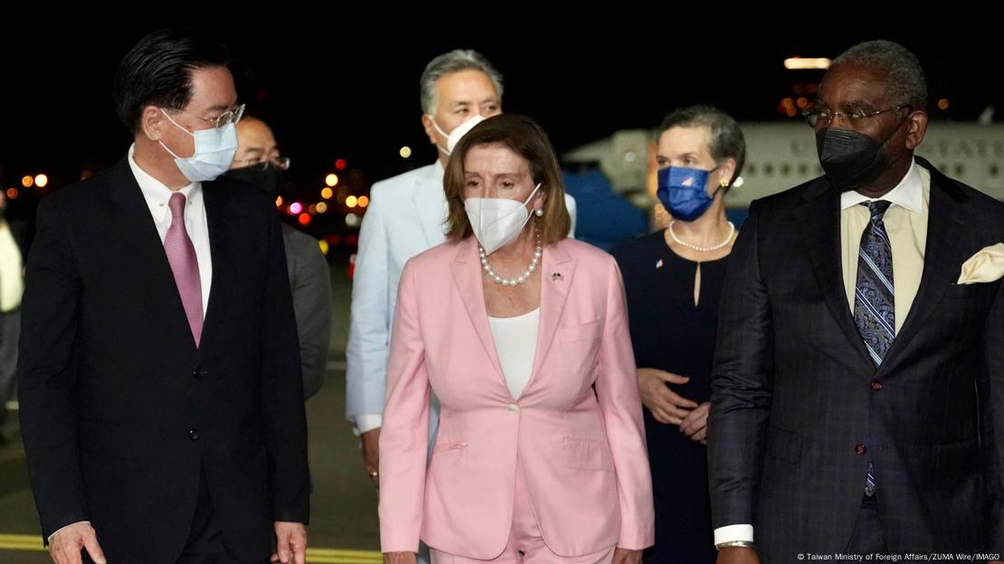 Nancy Pelosi de terno rosa e colar de pérolas, cerca por outras pessoas