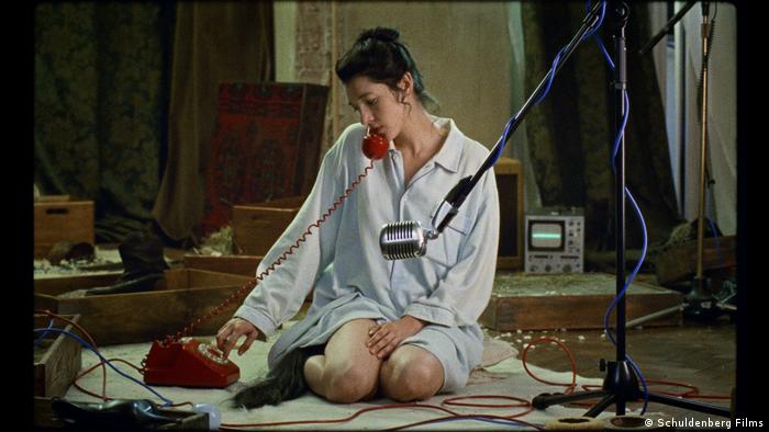 Eine Frau sitzt auf dem Boden und telefoniert mit einem alten Telefon, vor ihr steht ein Mikrofon.