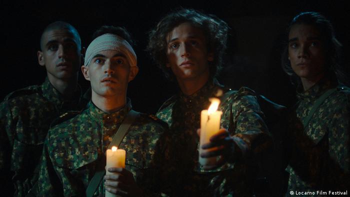 Filmszene: Fünf Personen stehen mit Kerzen in der Hand in der Dunkelheit und haben einen ernsten Gesichtsausdruck.