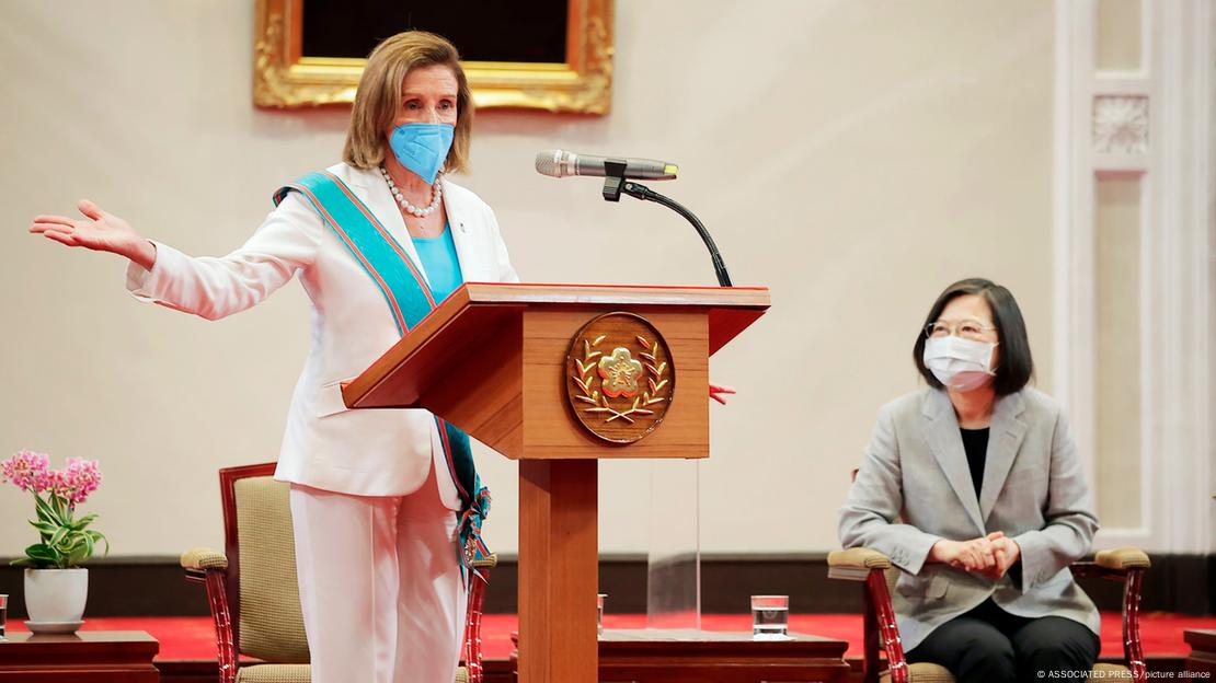 Nancy Pelosi fala em um púlpito. A presidente Tsai Ing-wen, sentada, observa