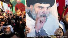 Followers of Shiite cleric Muqtada al-Sadr, displayed in a poster, chant pro-peace slogans in Basra, Iraq, Monday, Aug. 1, 2022. Iraqi security forces erected concrete barriers as panic took hold of the Iraqi street Monday ahead of counter-protests planned by Shiite political rivals that many feared could escalate to civil strife. (AP Photo/Nabil al-Jurani)
