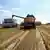 A harvester dumps grain into a truck during Ukraine's summer harvest