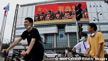 A large screen on a building showing promotion for the Chinese People's Liberation Army (PLA) is seen past cyclists in Beijing on August 4, 2022. - China's largest-ever military exercises encircling Taiwan kicked off August 4, in a show of force straddling vital international shipping lanes after a visit to the island by US House Speaker Nancy Pelosi. (Photo by Noel Celis / AFP) (Photo by NOEL CELIS/AFP via Getty Images)