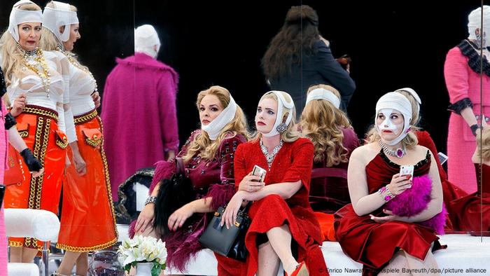 Women in fancy dresses and headbands sit on white sofas.