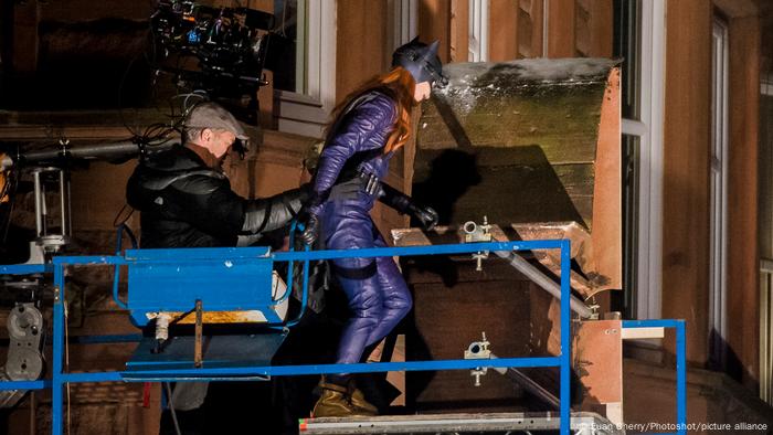 Dreharbeiten zu Batgirl, Mann hält Frau an den Hüften, sie steht in Batgirl-Kostüm auf einer Plattform