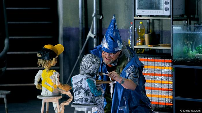 A mime disguised as a magician arranges his puppets.
