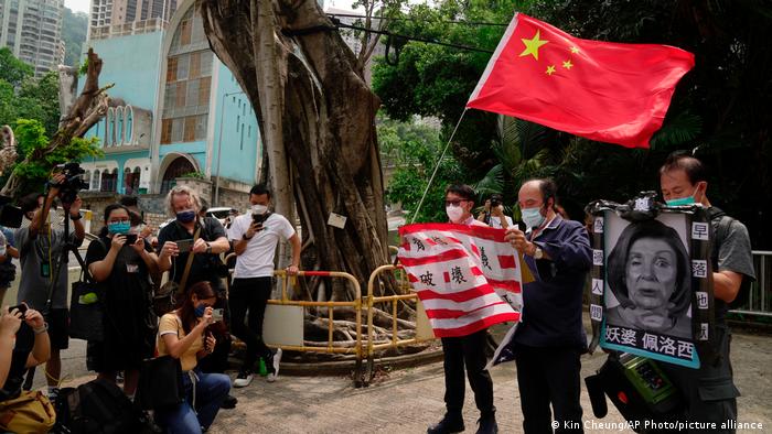 A Hong Kong, des manifestants tiennent un drapeau de la Chine et une photo de Nancy Pelosi face à des photographes pour dénoncer la visite de la leader démocrate