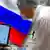 Cпециалист из России в белом халате перед монитором компьютера на фоне российского флага