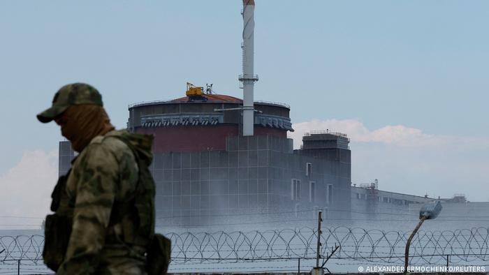 A soldier with a Russian flag on his uniform stands guard near the Zaporizhzhia power plant