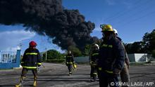 Firefighters are seen near an oil tank on fire in Matanzas, Cuba, on August 6, 2022. - The fire caused by lightning on Friday in a fuel depot in Matanzas, in western Cuba, spread to a second tank at dawn this Saturday and caused 49 injuries, official sources reported. (Photo by YAMIL LAGE / AFP)