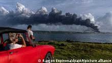 A photographer prepares to shoot a massive plume of smoke rising at Matanaz as a woman looks on from a car