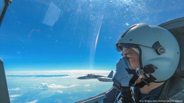 A Chinese pilot sits in the cockpit of a fighter jet, flying against a blue sky