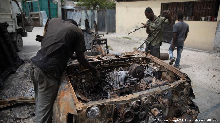 Haitian men rescuing parts from a charred car
