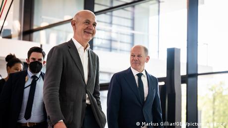Bernd Neuendorf and Olaf Scholz walk together unmasked; a man in a tie wears a mask