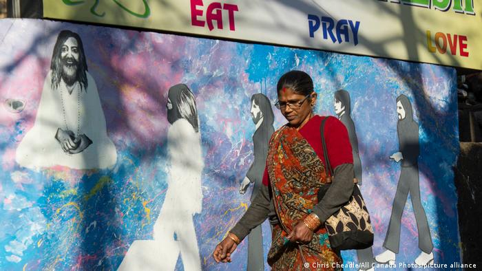 Eine Frau läuft durch die Straßen von Rishikesh - im Hintergrund eine bemalte Mauer