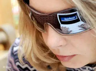 A laptop's browser displaying Facebook is reflected in a woman's sunglasses