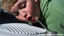 A boy in a green shirt drinking from a water fountain