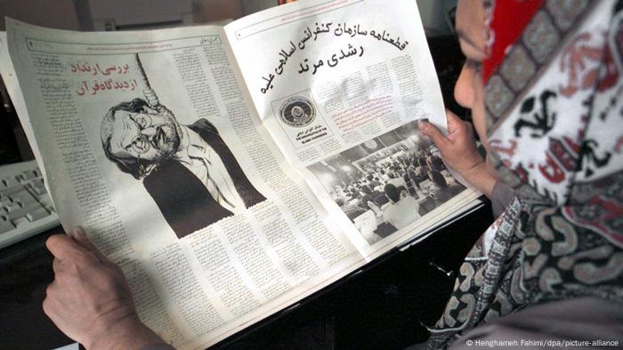 Una mujer lee un periódico iraní del año 2000, que muestra a Rushdie como un hombre colgado de una horca, luego de que las autoridades afirmaran que la fatua en su contra seguía vigente.