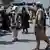Taliban-Männer gehen mit Schlagstöcken auf einige protestierende Frauenrechtlerinnen zu, die die Szene mit ihren Handys filmen. Im Bildhintergrund sind westliche Journalisten zu sehen