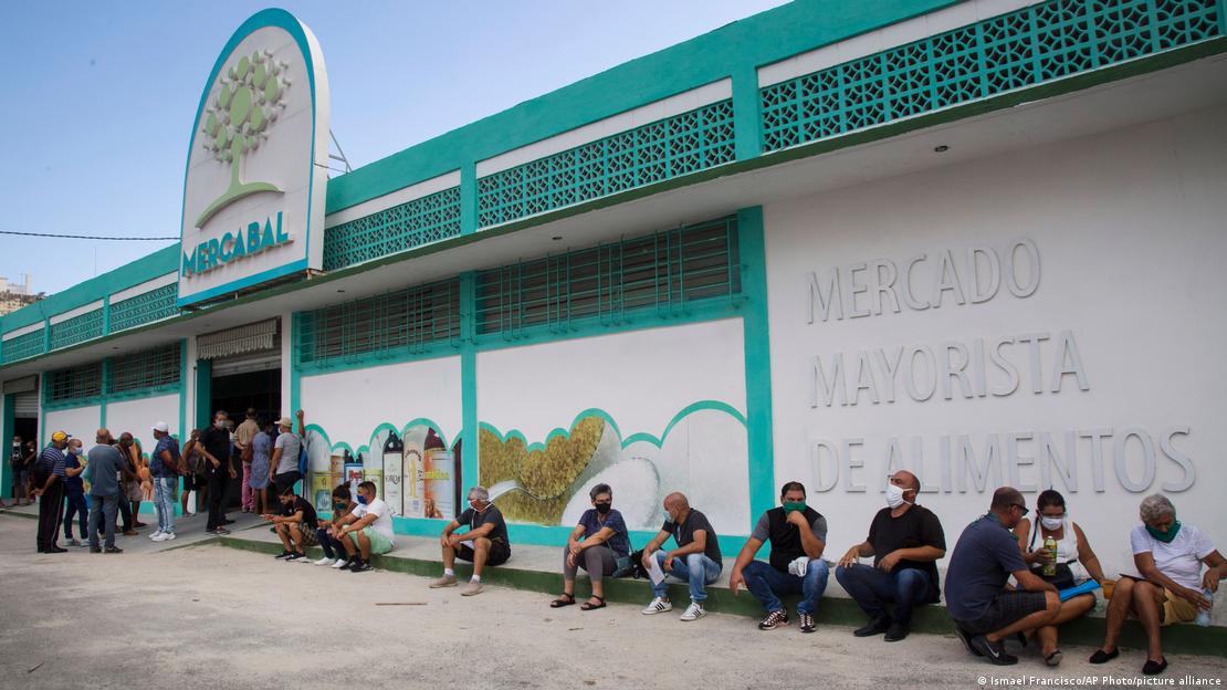 Gente sentada fuera de un mercado mayorista, en La Habana.