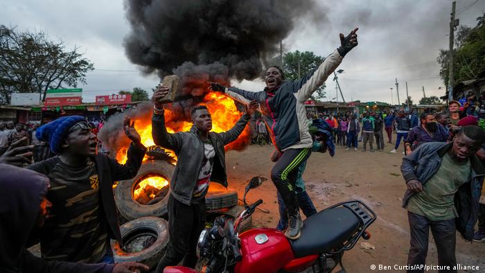 Mehrere Demonstranten recken vor brennenden Autoreifen die Arme in die Höhe