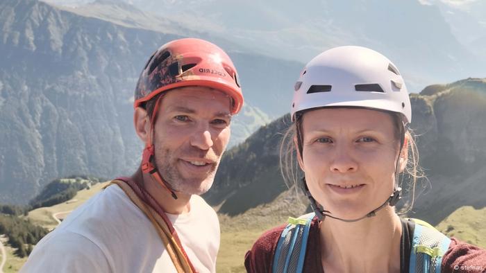 Mann und Frau mit Helm und Kletterausrüstung vor Bergen, Schweiz