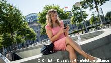 ILLUSTRATION - Eine Frau sitzt am 11.08.2020 in Berlin auf einer Mauer und schaut auf ein Smartphone (gestellte Szene). Foto: Christin Klose || Modellfreigabe vorhanden