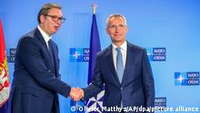 NATO chief Jens Soltenberg and Serbian President Aleksandar Vucic shaking hands in front of NATO and Serbian flags