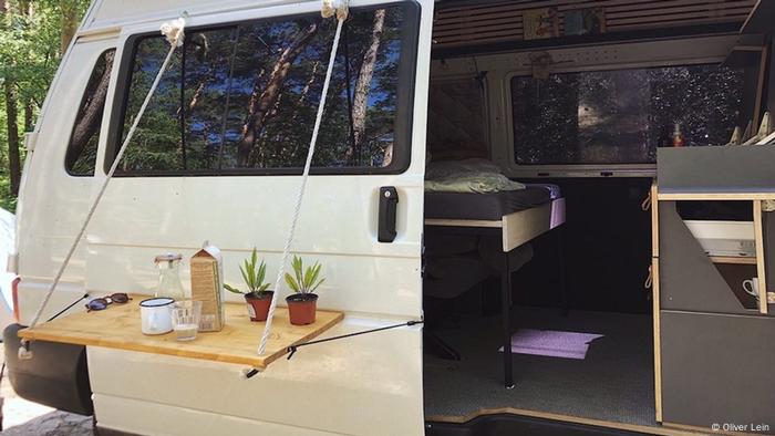 Le côté d'un camping-car avec une table de petit-déjeuner attachée à la porte latérale ouverte à travers laquelle un lit peut être vu